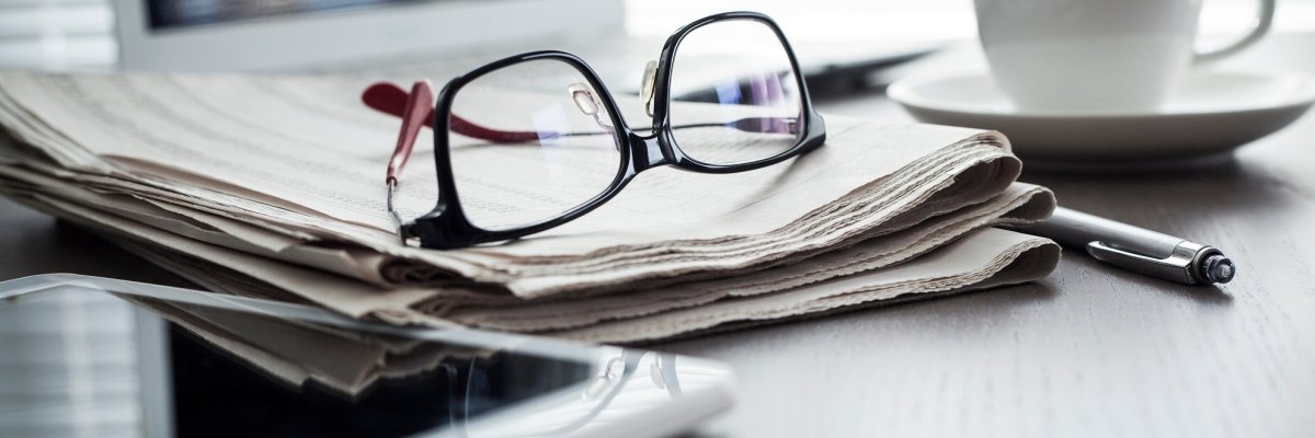 Eine Zeitung, eine Brille, ein Tablet und ein Kugelschreiber auf einem Tisch