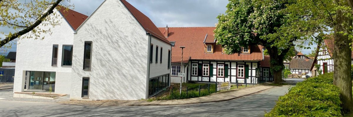 Ein modernes, weiß geklinkertes Gebäude mit schmalen Fenstern und einem dahinterliegenden historischen Fachwerkhaus.