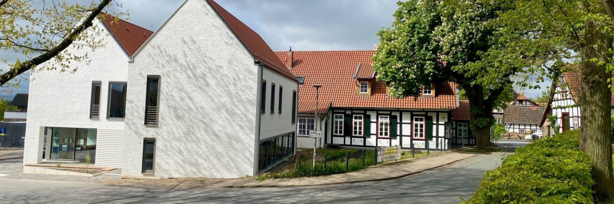 Ein modernes, weiß geklinkertes Gebäude mit schmalen Fenstern und einem dahinterliegenden historischen Fachwerkhaus.