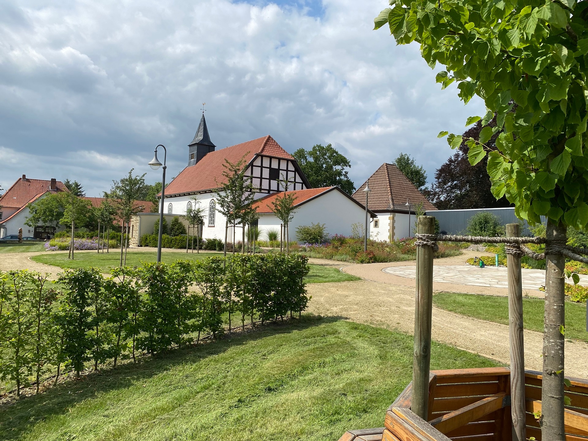 Ein bepflanzter Dorfplatz mit einer historischen Kapelle im Hintergrund.