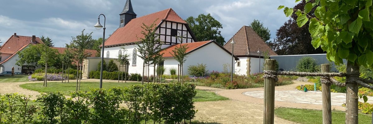 Ein bepflanzter Dorfplatz mit einer historischen Kapelle im Hintergrund.