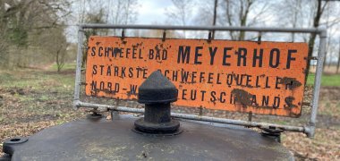 Schwefelquelle Levern Ein alter Brunnendeckel eines Schwefelbrunnens mit einem gelben Schild auf dem der Name der Schwefelquelle steht.