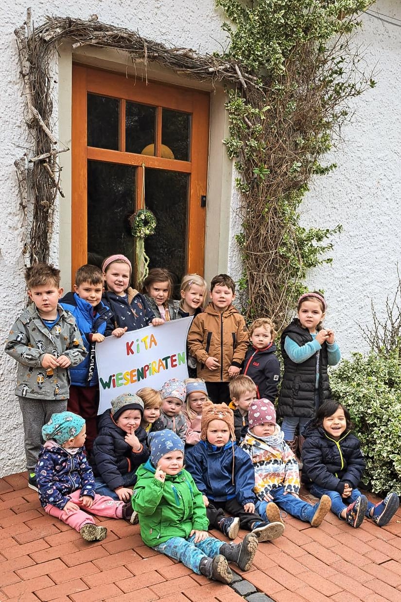 Kinder eines Kindergartens, die ein Schild mit der Aufschrift "Kita Wiesenpiraten" hochhalten.