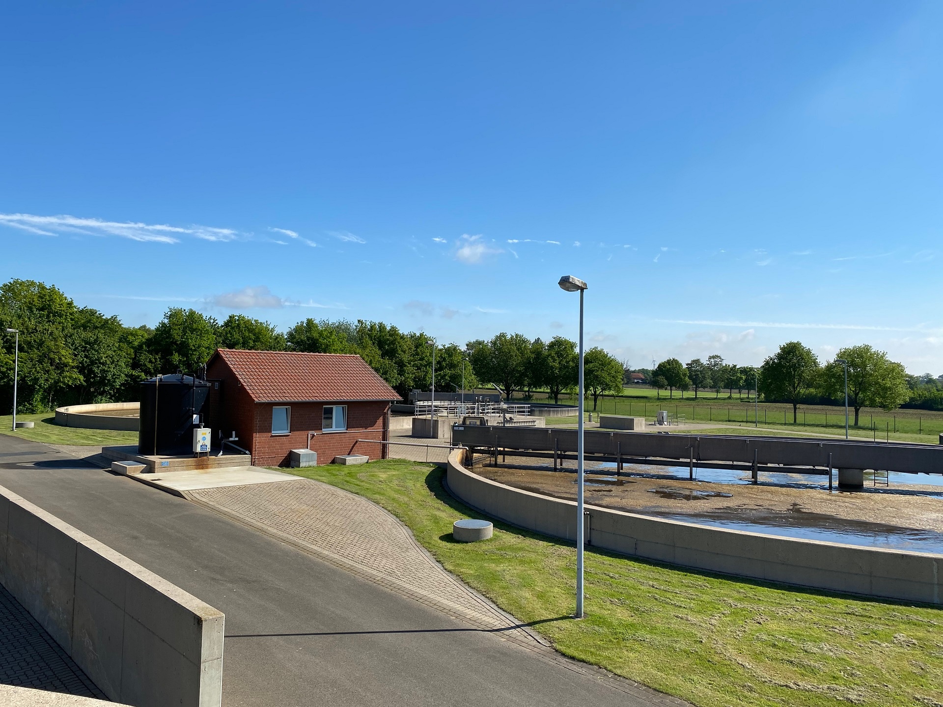 Blick auf zwei Klärbecken und ein rotes Pumpenhäuschen einer Kläranlage. 