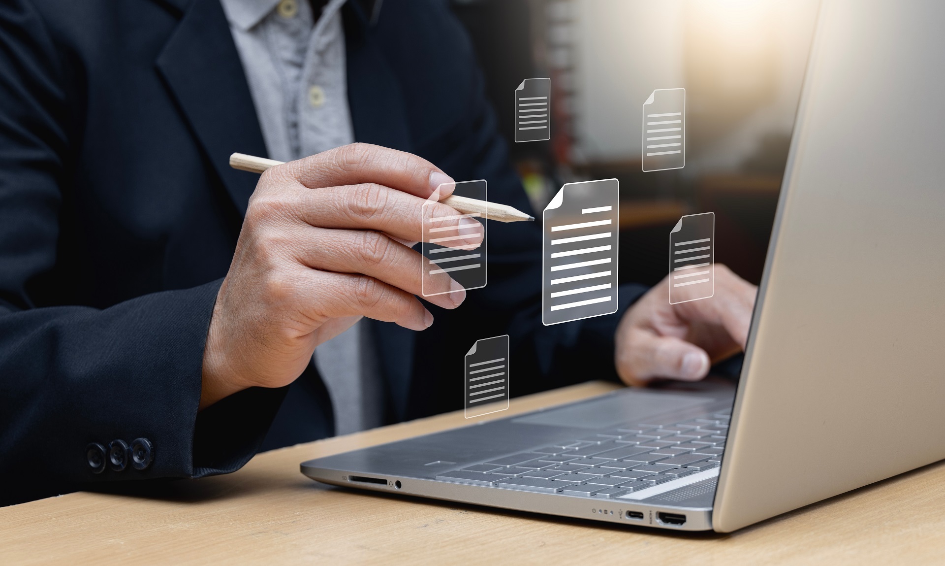 Ein Mann an einem Laptop. Im Foto sind Illustrationen von Akten zu sehen. Das Bild soll die Transformation vom Aktenvorgang zu einem digitalen Prozess verdeutlichen.