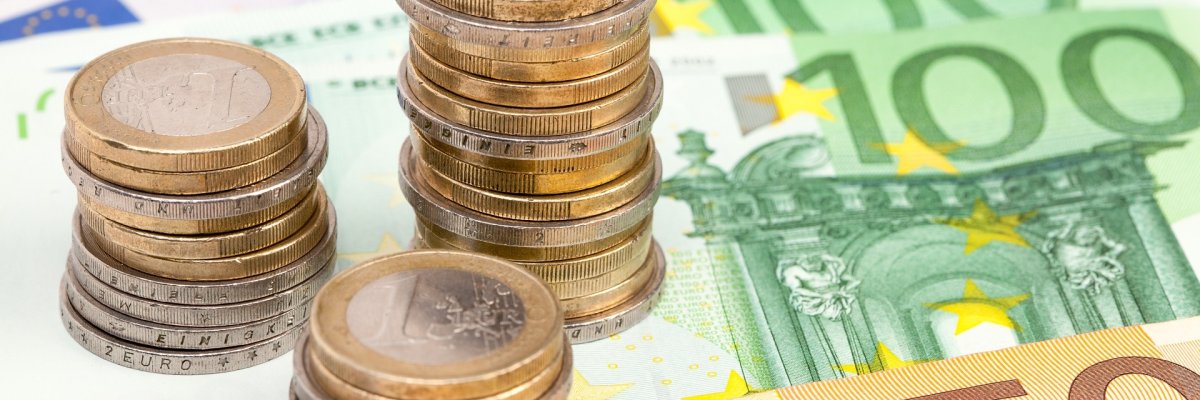 Nahaufnahme mehrerer 50-Euro-, 100-Euro- und 500-Euro-Scheine sowie mehrerer gestapelter Euromünzen.