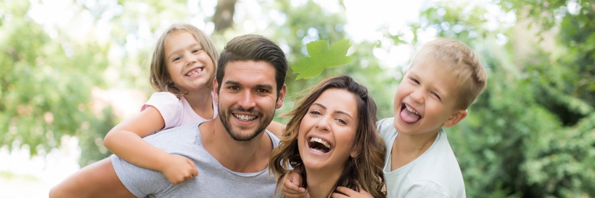 Familie im Urlaub Eine glückliche Familie im Sommer. Mutter und Vater tragen jeweils ein Kind huckepack.