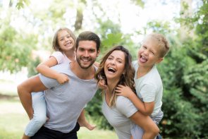 Familie im Urlaub Eine glückliche Familie im Sommer. Mutter und Vater tragen jeweils ein Kind huckepack.