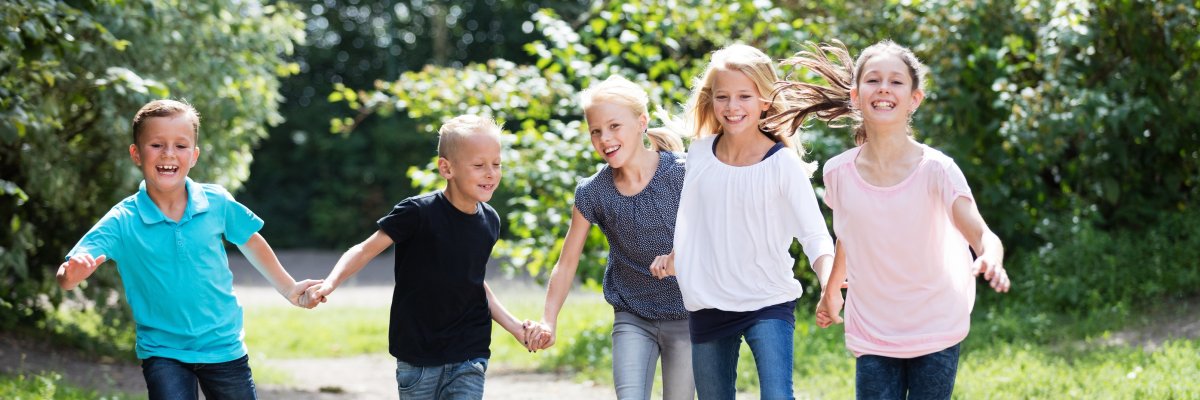 Kinder laufen auf dem Schulhof Fünf etwa 10-jährige Kinder laufen lachend und sich an der Hand haltend durch einen Garten.