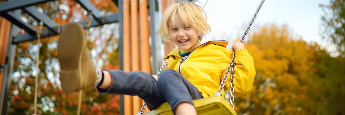 Ein Junge, in einer gelben Regenjacke, der auf einer Schaukel schwingt. 