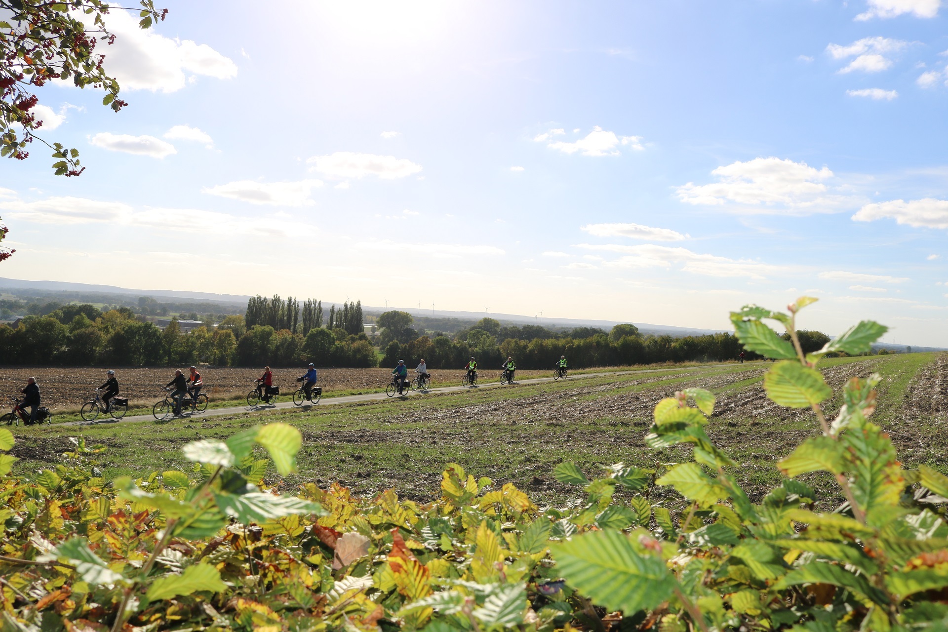 Fahrradtour Ein Panoramablick in eine sommerliche Landschaft. Zu erkennen sind mehrere, mit Warnweste gekleidete Teilnehmerinnen und Teilnehmer einer Fahrradtour.