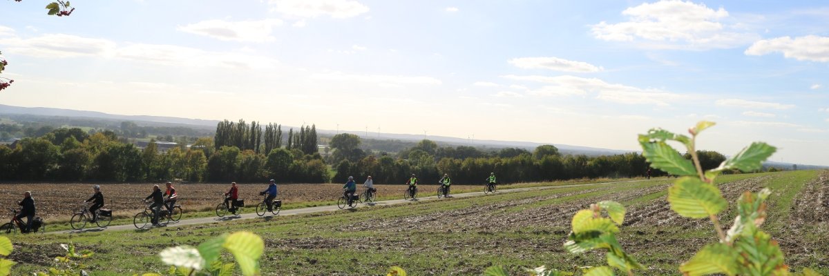 Fahrradtour Ein Panoramablick in eine sommerliche Landschaft. Zu erkennen sind mehrere, mit Warnweste gekleidete Teilnehmerinnen und Teilnehmer einer Fahrradtour.