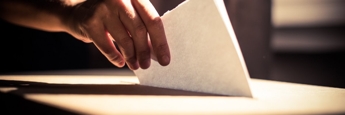 Wahl Eine Nahaufnahme einer Hand, die einen Wahlschein in die Wahlurne wirft.