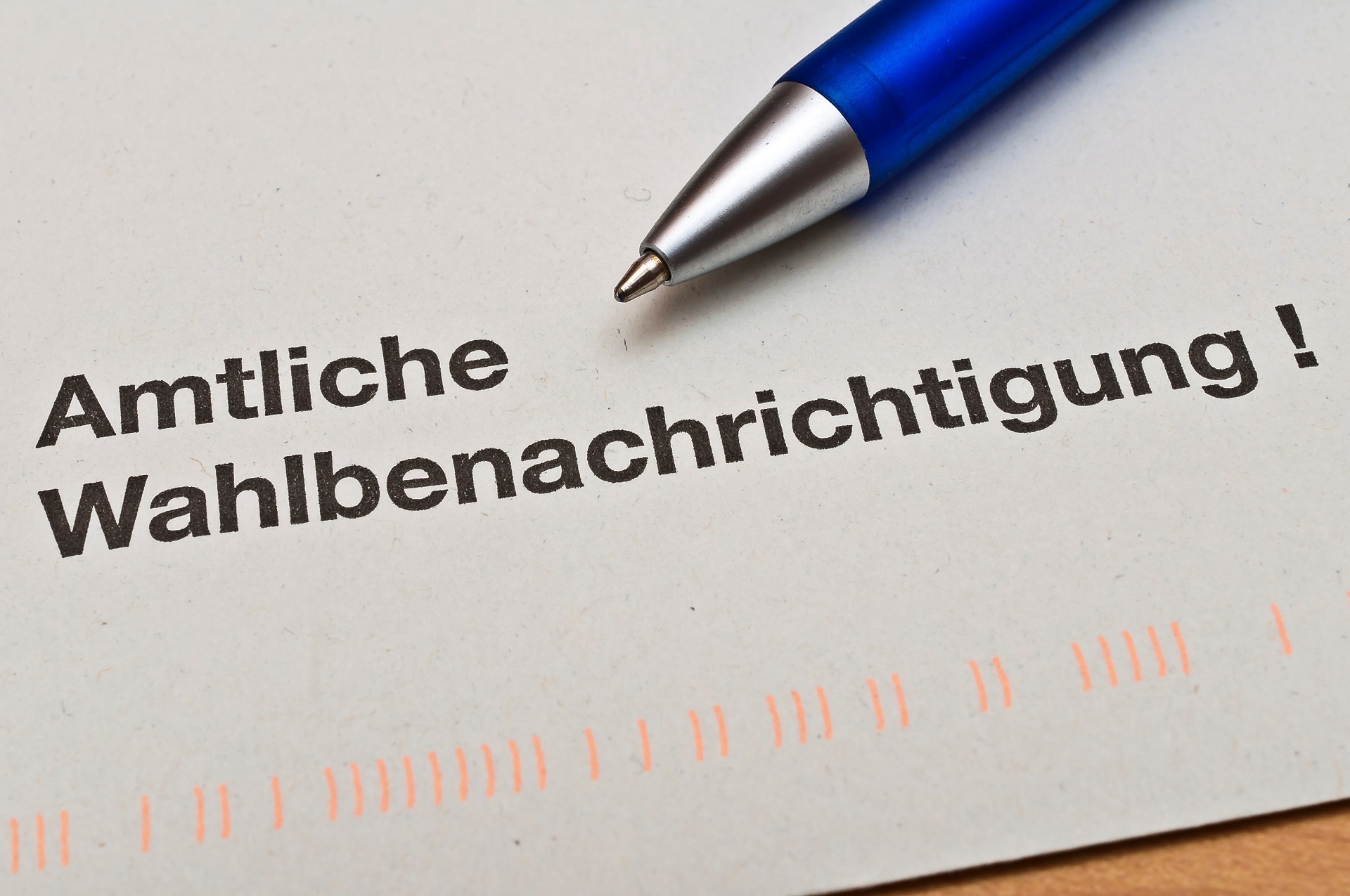 Eine Nahaufnahme eines Briefumschlages, der mit den Worten Amtliche Wahlbenachrichtigung und auf dem ein blauer Kugelschreiber liegt.