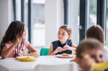 A group of cheerful small school kids in canteen, eating lunch. Einige Kinder, die gerade in einer Schulmensa beim Essen sind.