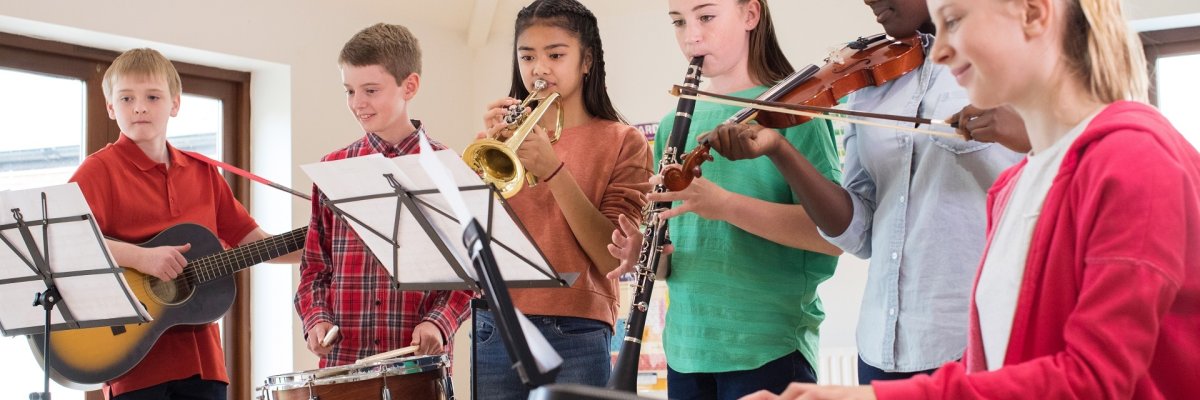 Eine Gruppe von Kindern, die gemeinsam musiziert. Díe Kinder spielen verschiedene Instrumente, wie Trommel, Geige, Gitarre, Trompete und Keyboard.