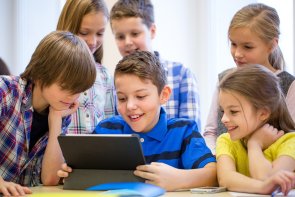 Schüler mit Tablet Eine Gruppe von jungen Schülern, die einem Mitschüler über die Schulter gucken, der an einem Tablett arbeitet.