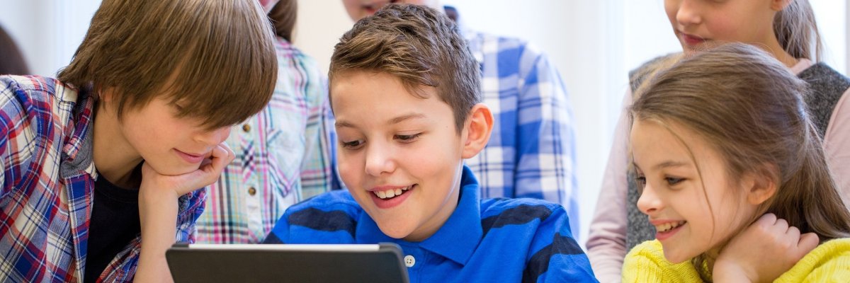 Eine Gruppe von jungen Schülern, die einem Mitschüler über die Schulter gucken, der an einem Tablett arbeitet. 