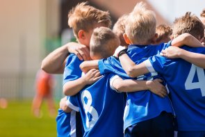 Kids Play Sports. Children Sports Team United Ready to Play Game. Children Team Sport. Youth Sports For Children. Boys in Sports Uniforms. Young Boys in Soccer Sportswear Spieler einer Kinderfußballmannschaft in blauen Trikots liegen sich in den Armen und freuen sich.