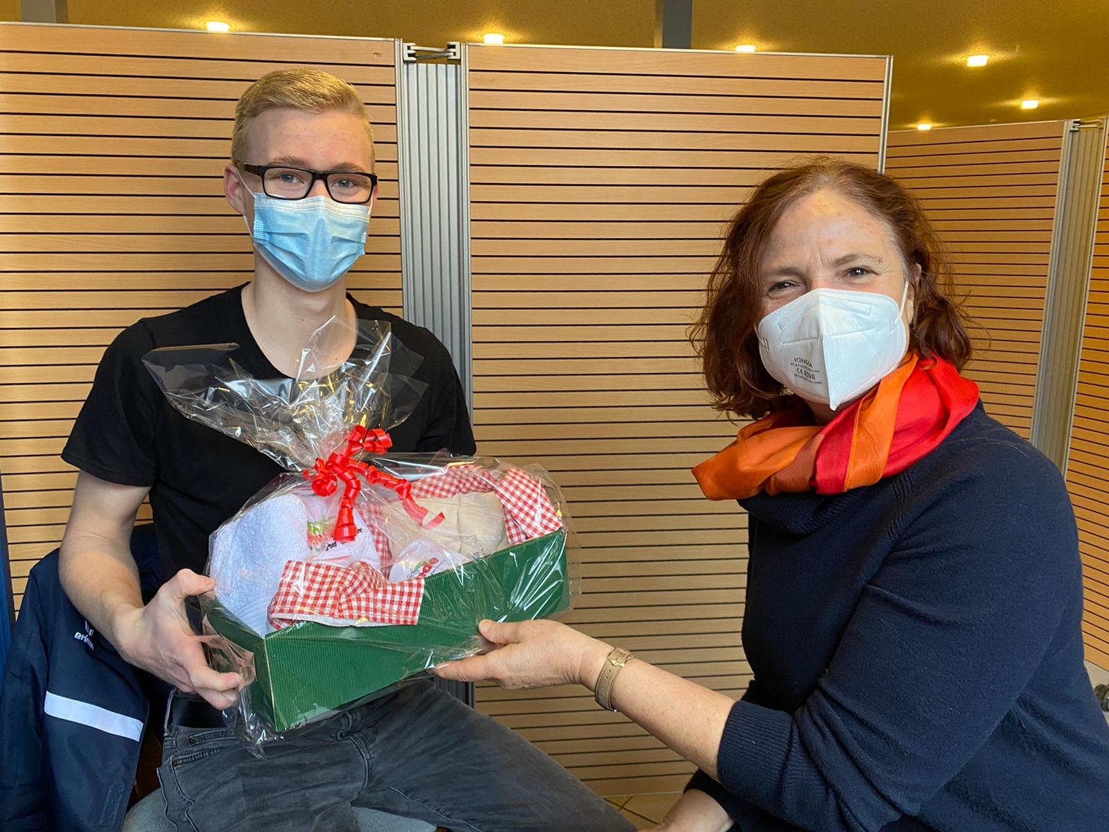 Eine Ärztin überreicht einem jungen Mann ein Geschenk. 