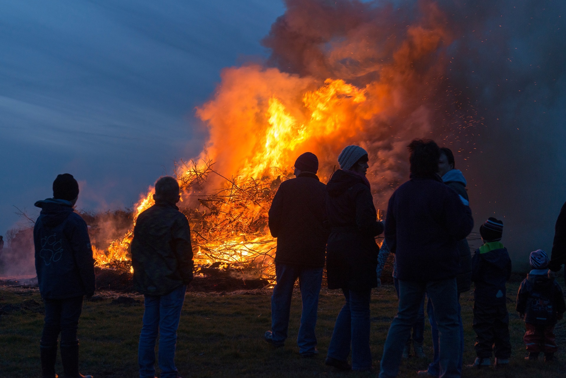 Mehrere Personen, die vor einem Brauchtumsfeuer stehen. 