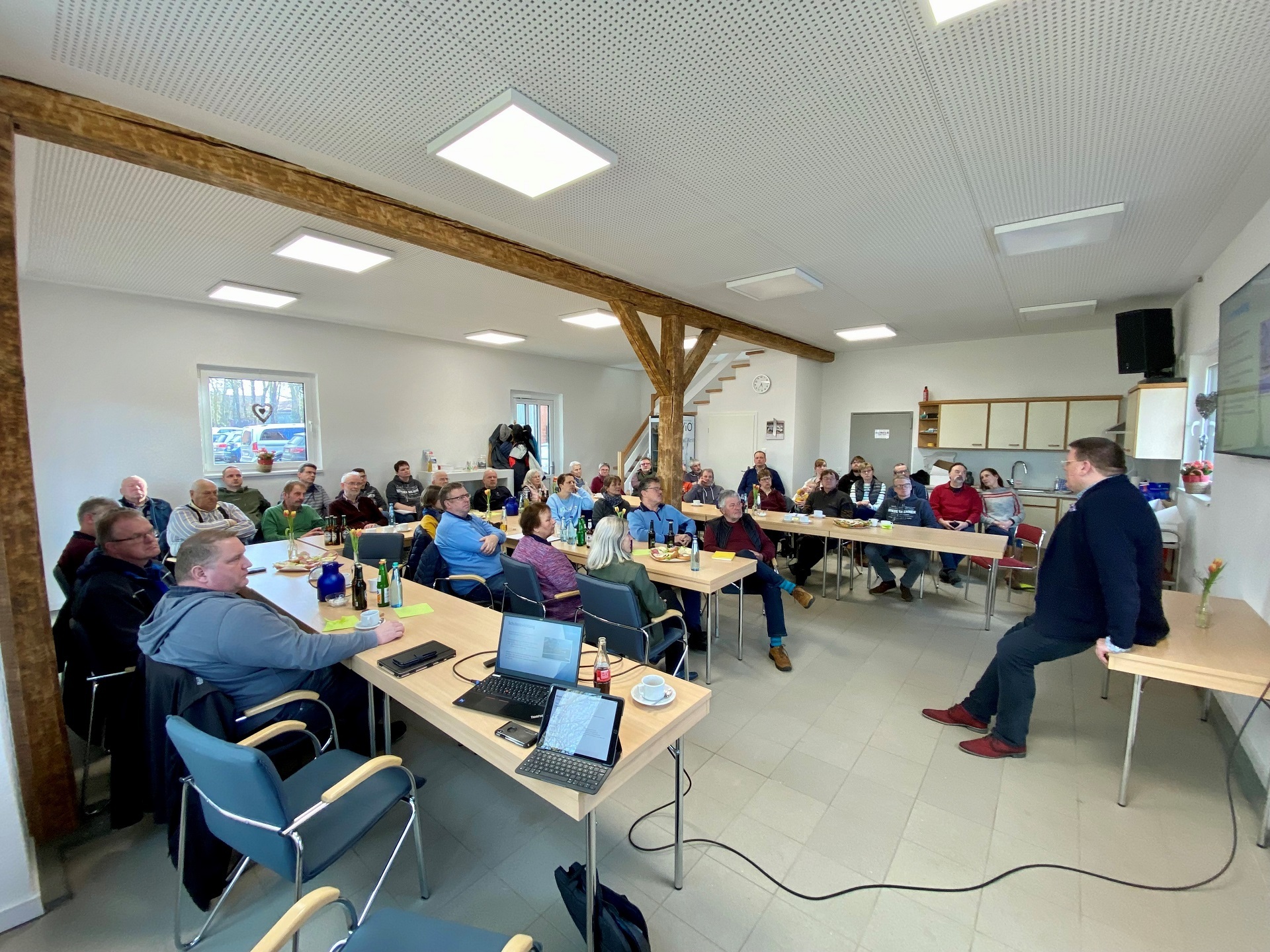 Ein mit vielen Personen gefüllter Raum, die einem Sprecher zuhören. 
