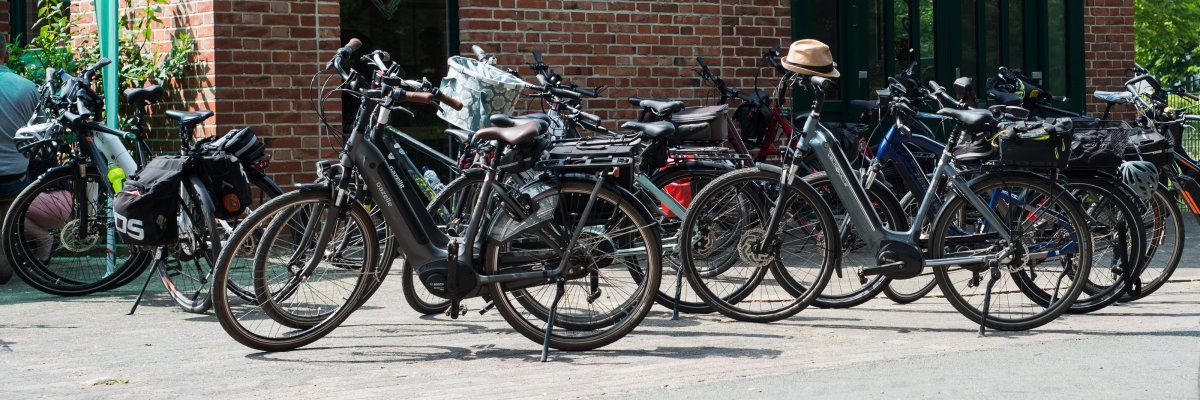 Mehrere abgestellte Fahrräder und E-Bikes vor einem rot geklinkerten Gebäude. 