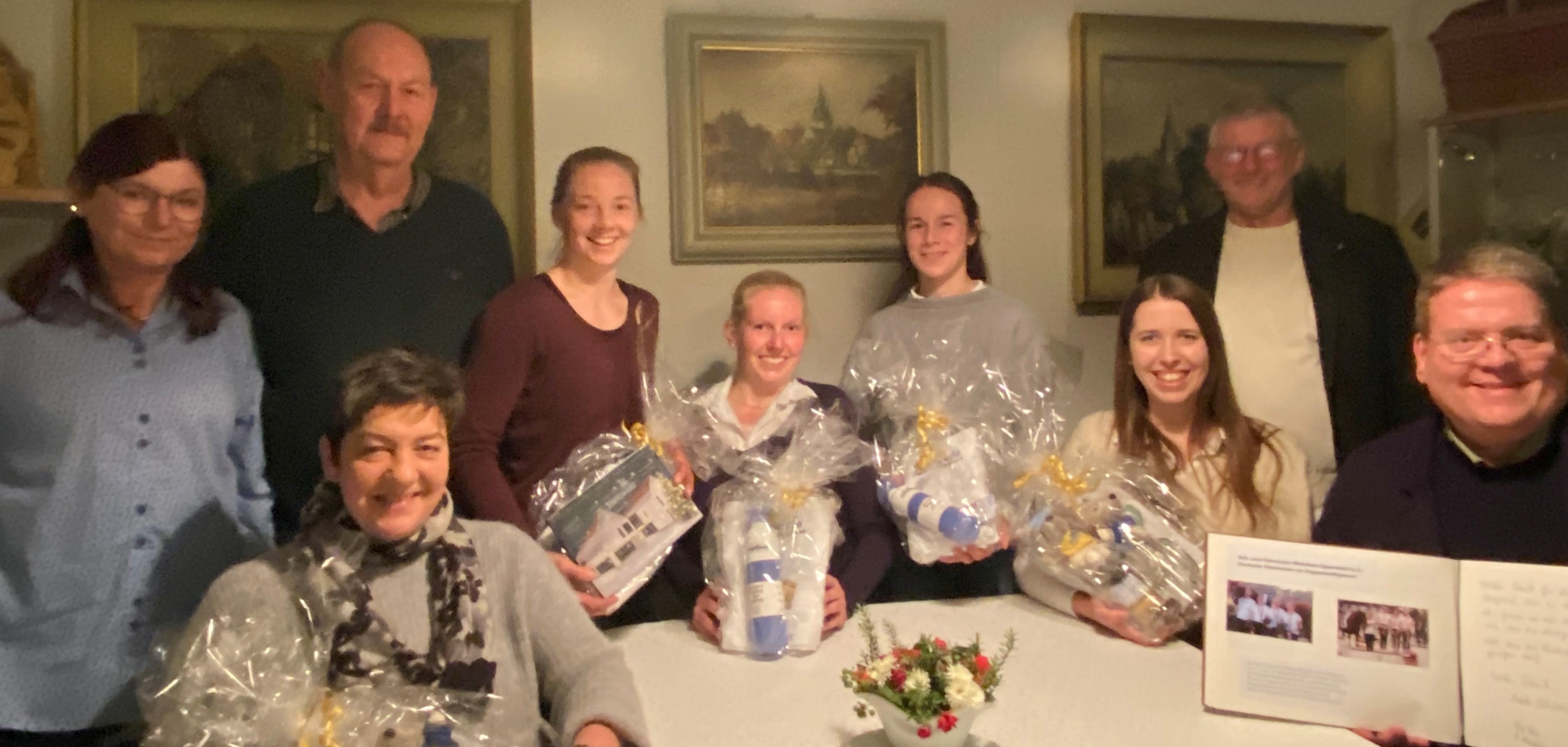 Insgesamt neun Personen sitzen bei gedimmten Licht in einem historischen Wohnzimmer.