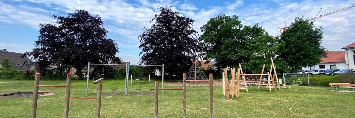 Verschiedene Spielgeräte, wie eine Turnstange und ein Klettergerüst auf einem Spielplatz. 