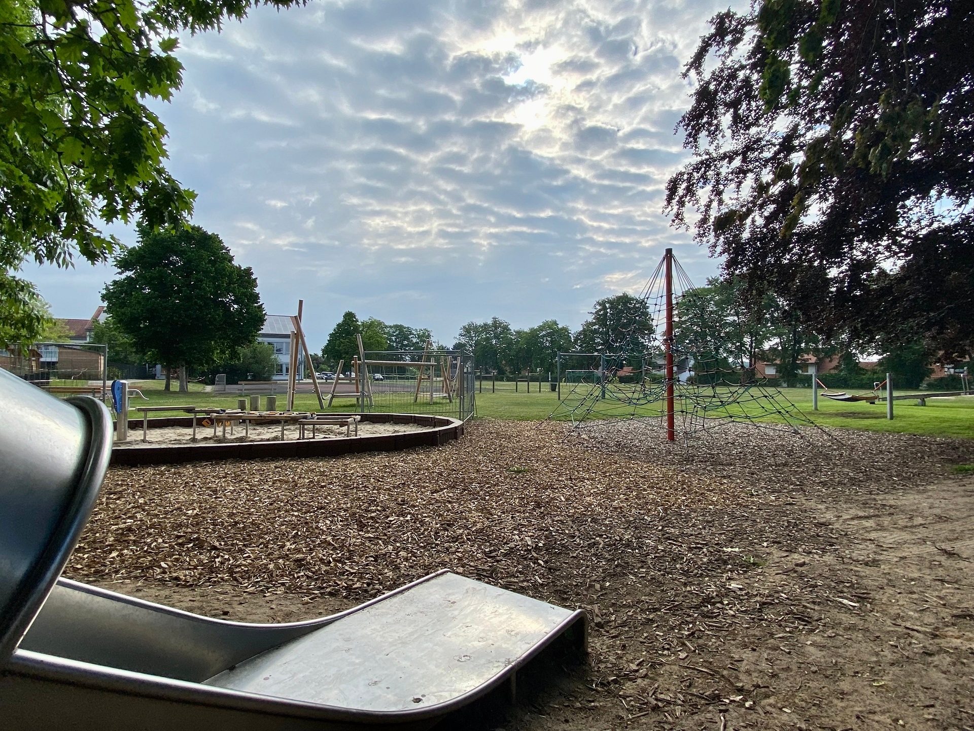 Ein Spielplatz mit verschiedenen Spielgeräten, wie Sandkasten, Rutsche und Turnstangen. 
