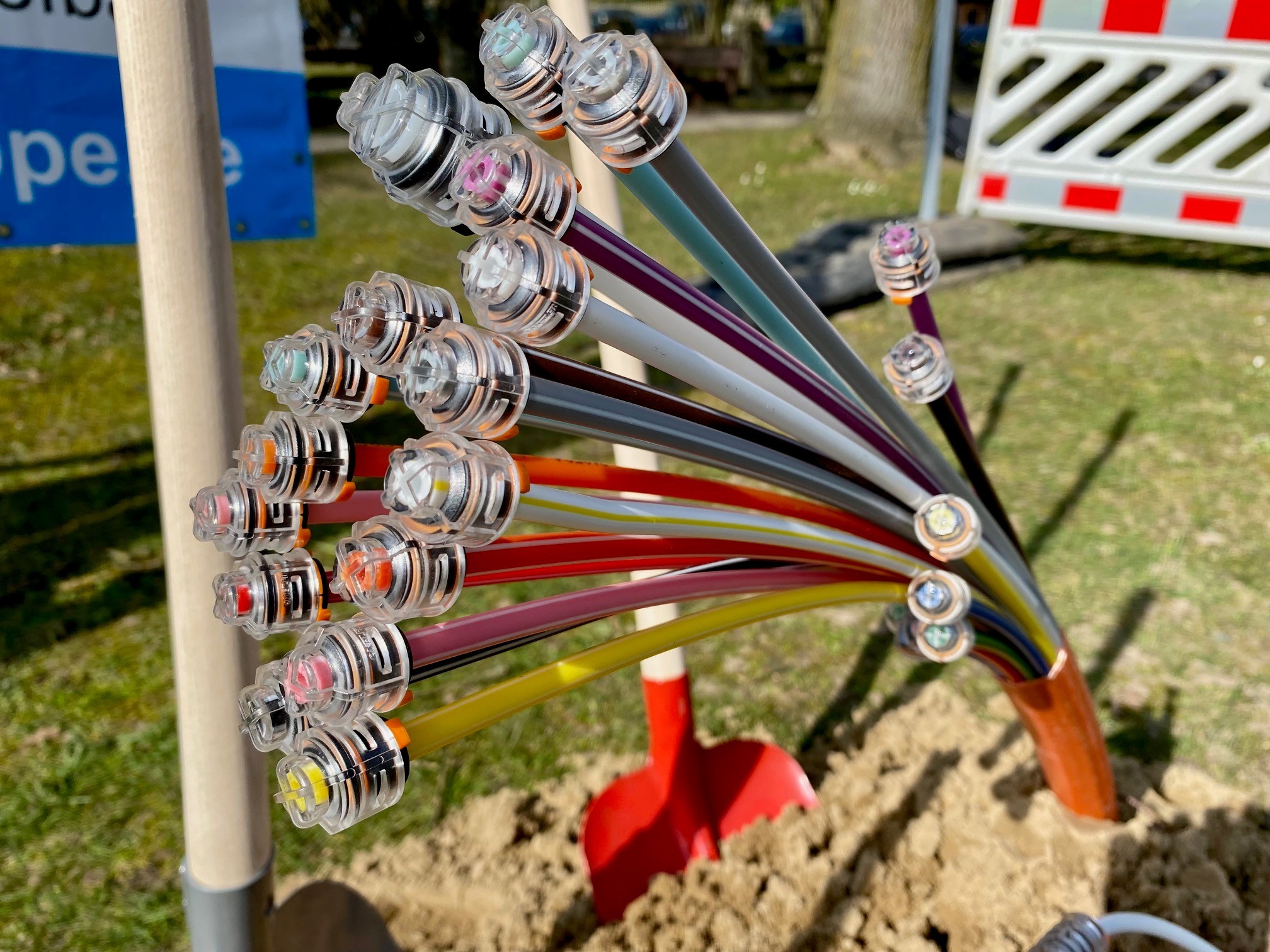 Ein Strang mit vielen bunten Röhrchen ragt aus der Erde. Es handelt sich um Glasfaserkabel. 