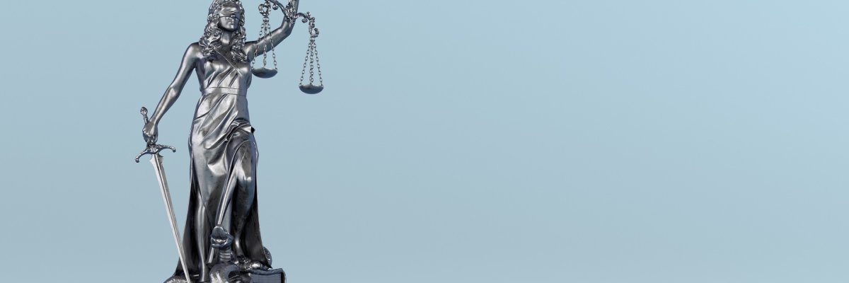 Justizia Eine silberne Justizia-Statur vor einem hellblauen Hintergrund.