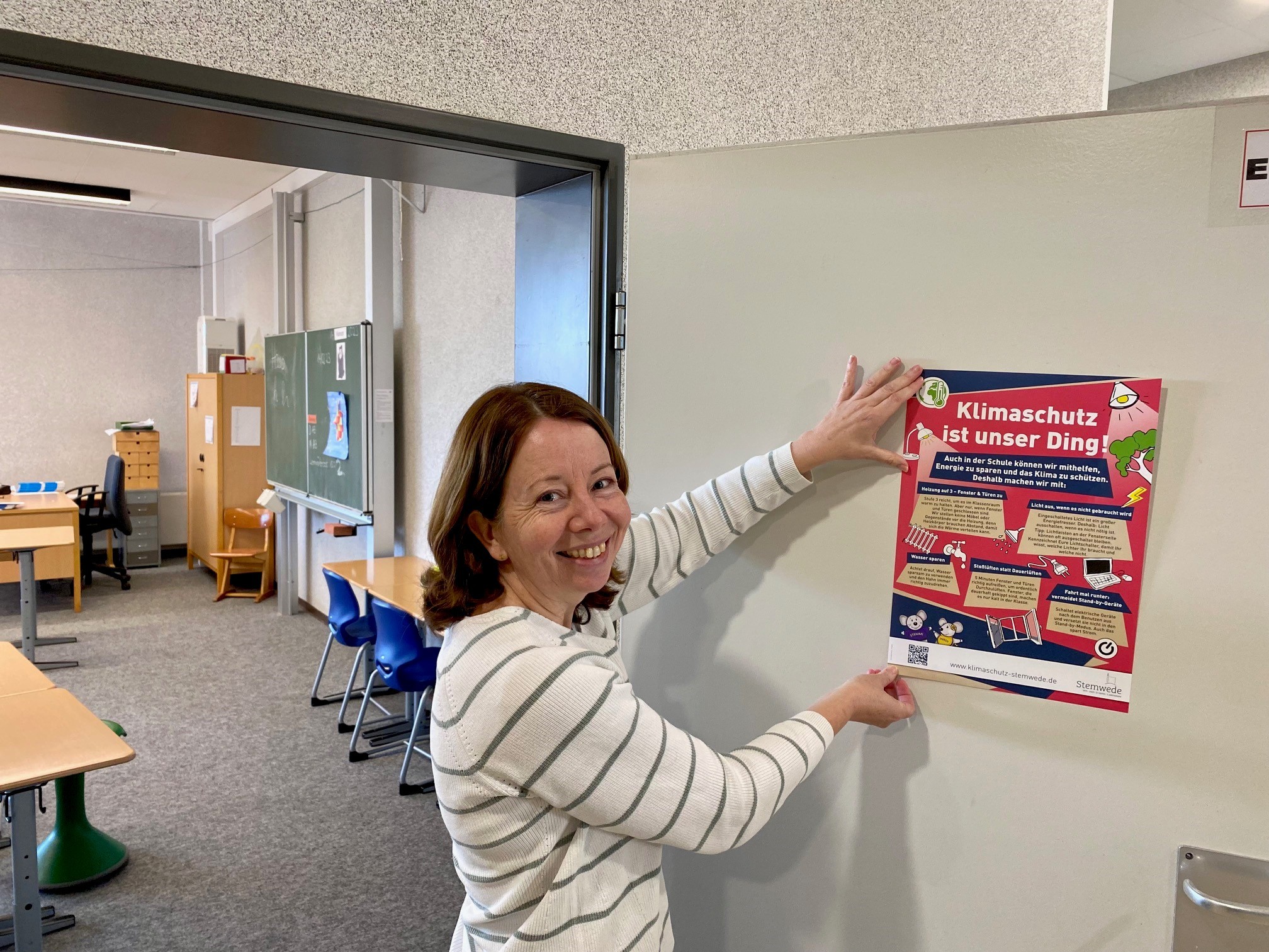 Eine Frau hängt ein Plakat mit Tipps zum Energiesparen an die Tür eines Klassenraums.
