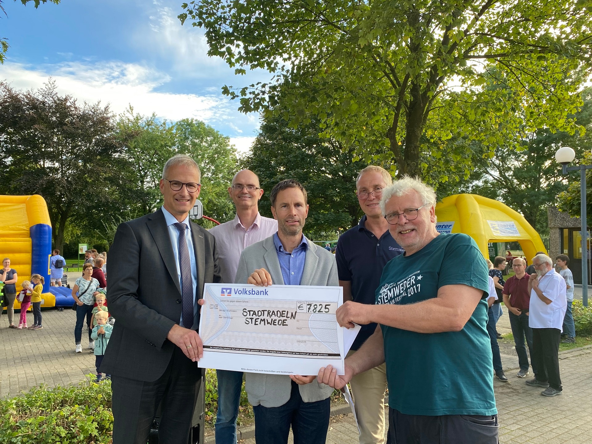 Fünf Männer, die in die Kamera lächeln und einen überdimensionalen, symbolischen Scheck in die Kamera halten.