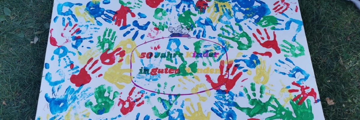 Eine Leinwand, auf der viele bunte Abdrücke von Kinderhänden sowie der Schriftzug "50 Jahre Kinder in guten Händen" zu sehen sind.