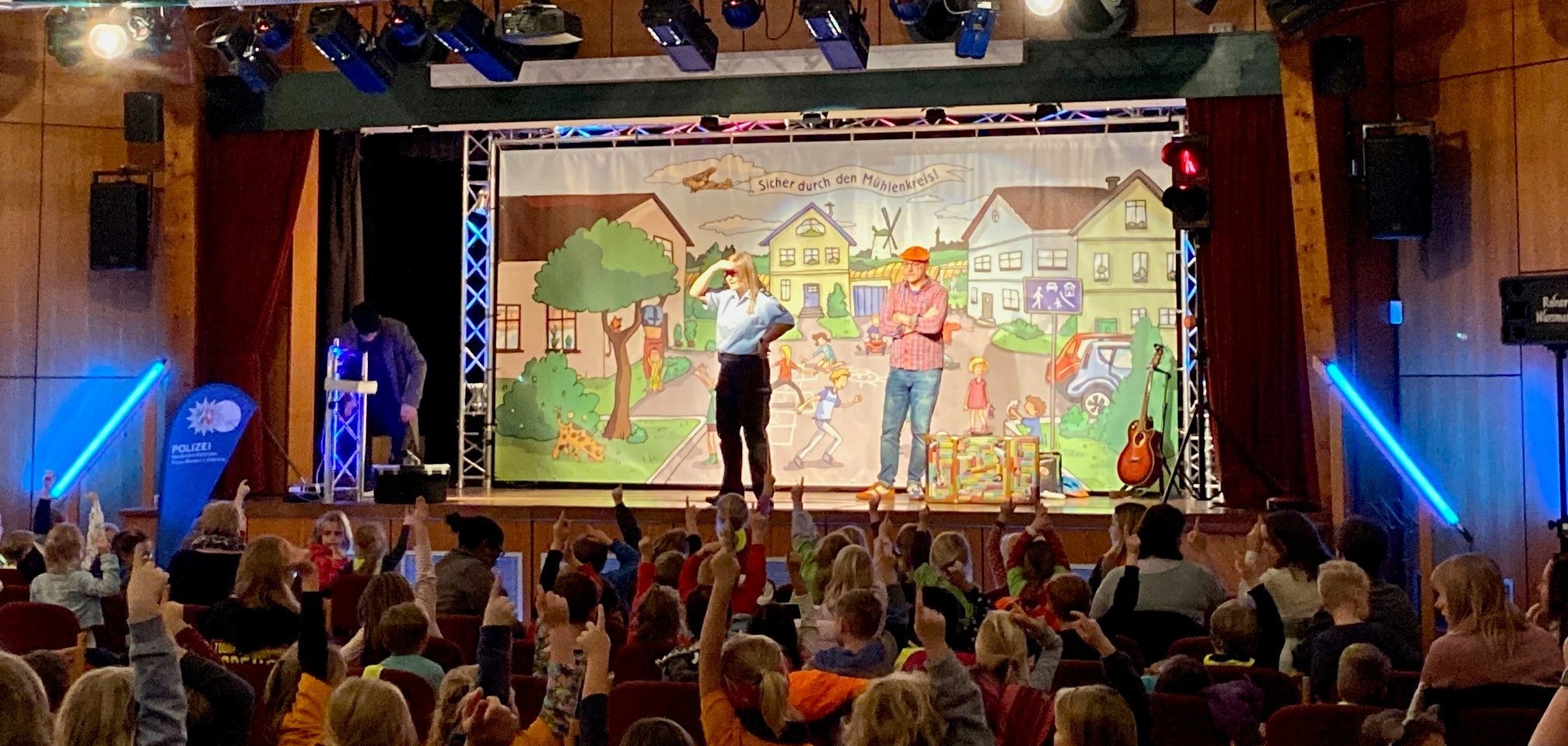 Eine Veranstaltung, bei der viele Kinder im Publikum sitzen, während auf der Bühne zwei Menschen etwas vorführen.