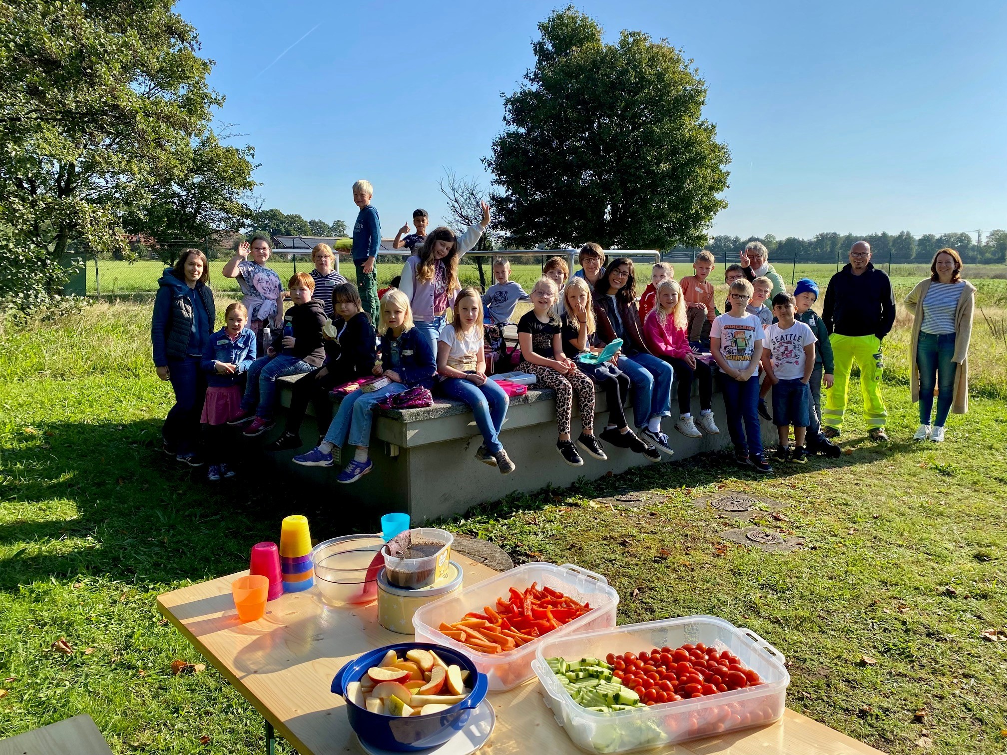 Eine Kindergartengruppe, die auf einer Wiese eines Wasserwerkes ein Picknick macht.