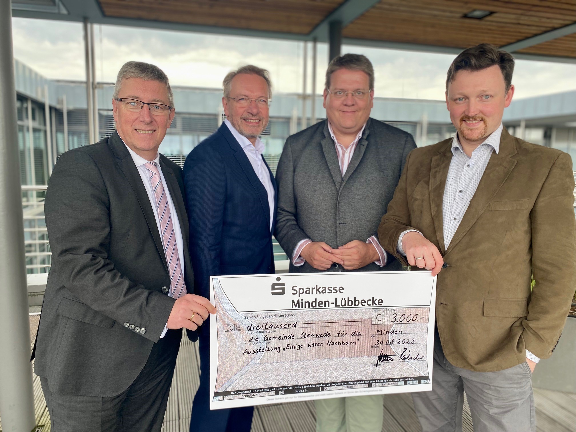 Vier Männer halten einen symbolischen Scheck in die Höhe. 