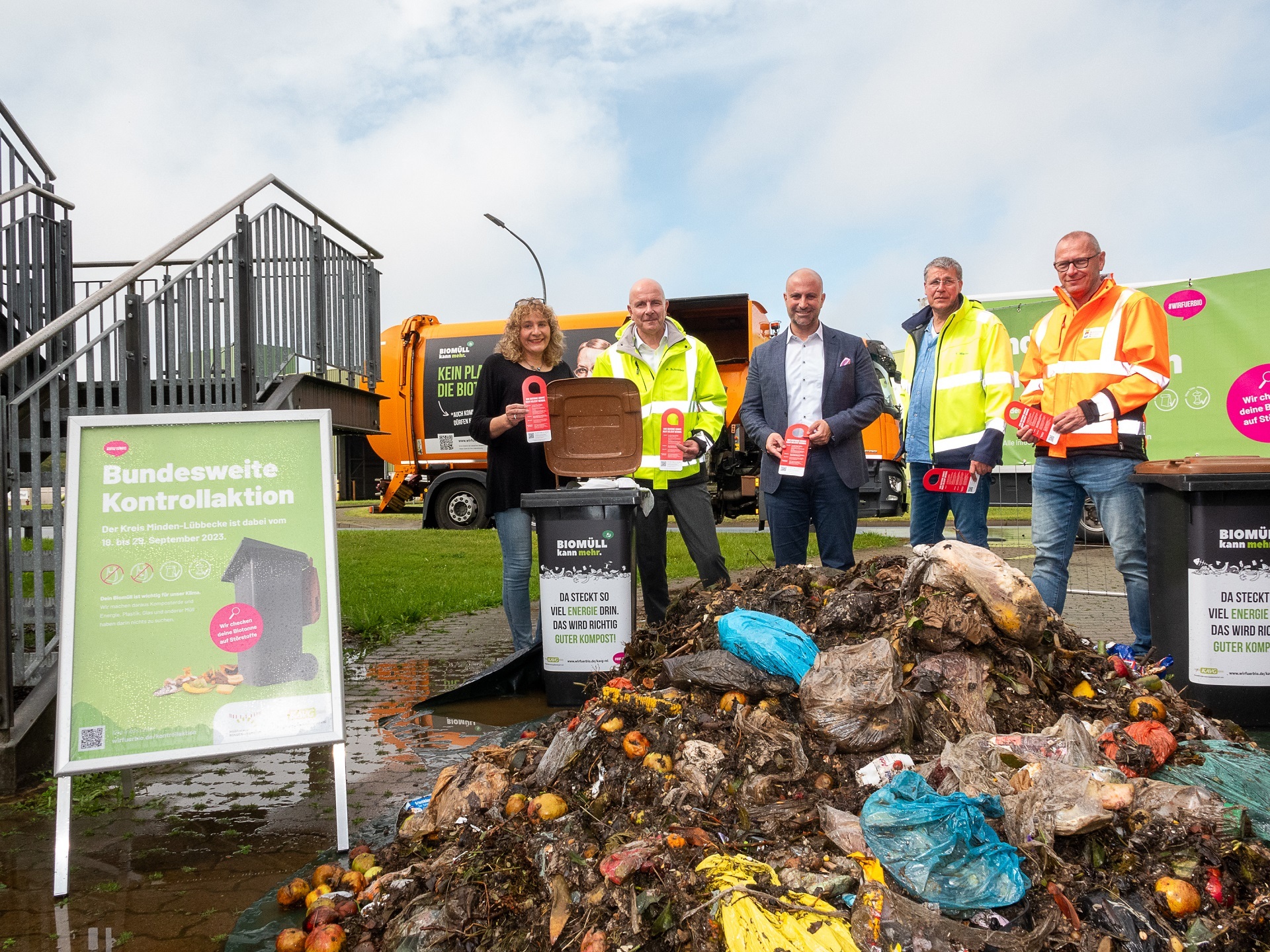 Gruppenfoto von vier Männern und einer Frau, die hinter einem Haufen Biomüll stehen, in dem viel Plastikstörstoffe zu erkennen ist.  