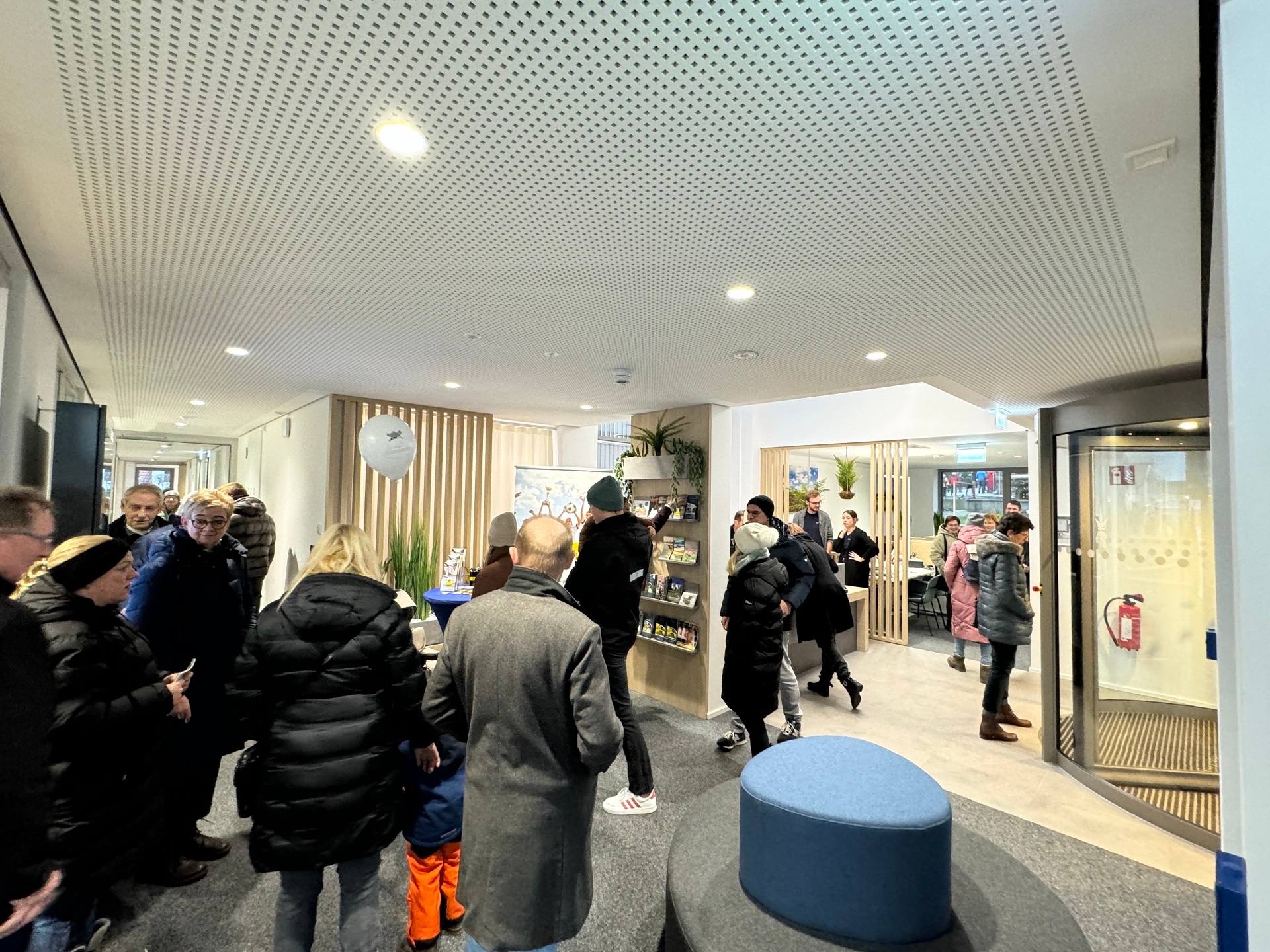 Zahlreiche Personen, die Winterjacken und Mäntel tragen in einem Empfangsbereich, der dadurch recht eng und voll wirkt.