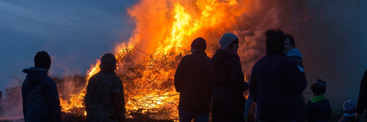 Ein großes Osterfeuer. Mehrere Menschen stehen davor und beobachten das Feuer.