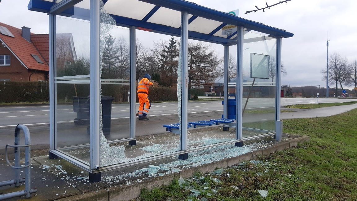 Ein zerstörtes, gläsernes Buswartehäuschen an einer Straße. Überall liegen Scherben.
