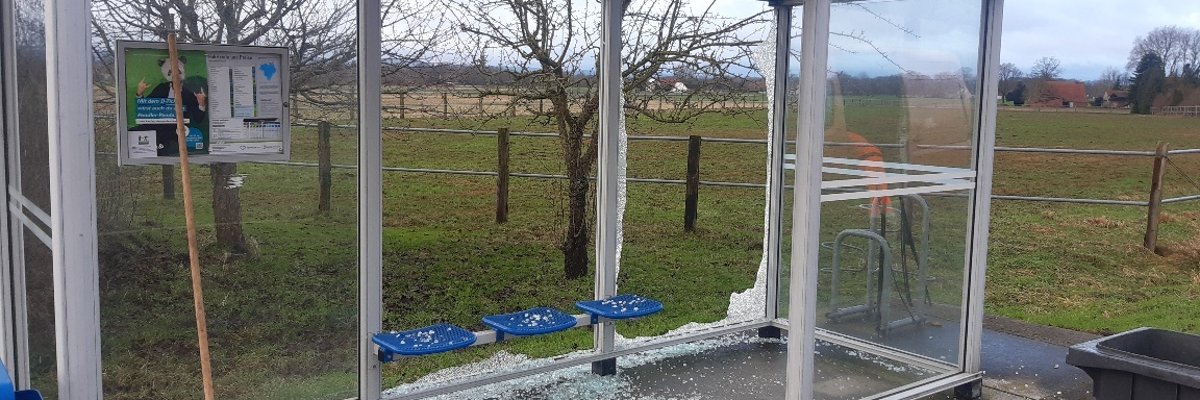 Ein zerstörtes, gläsernes Buswartehäuschen an einer Straße. Überall liegen Scherben.