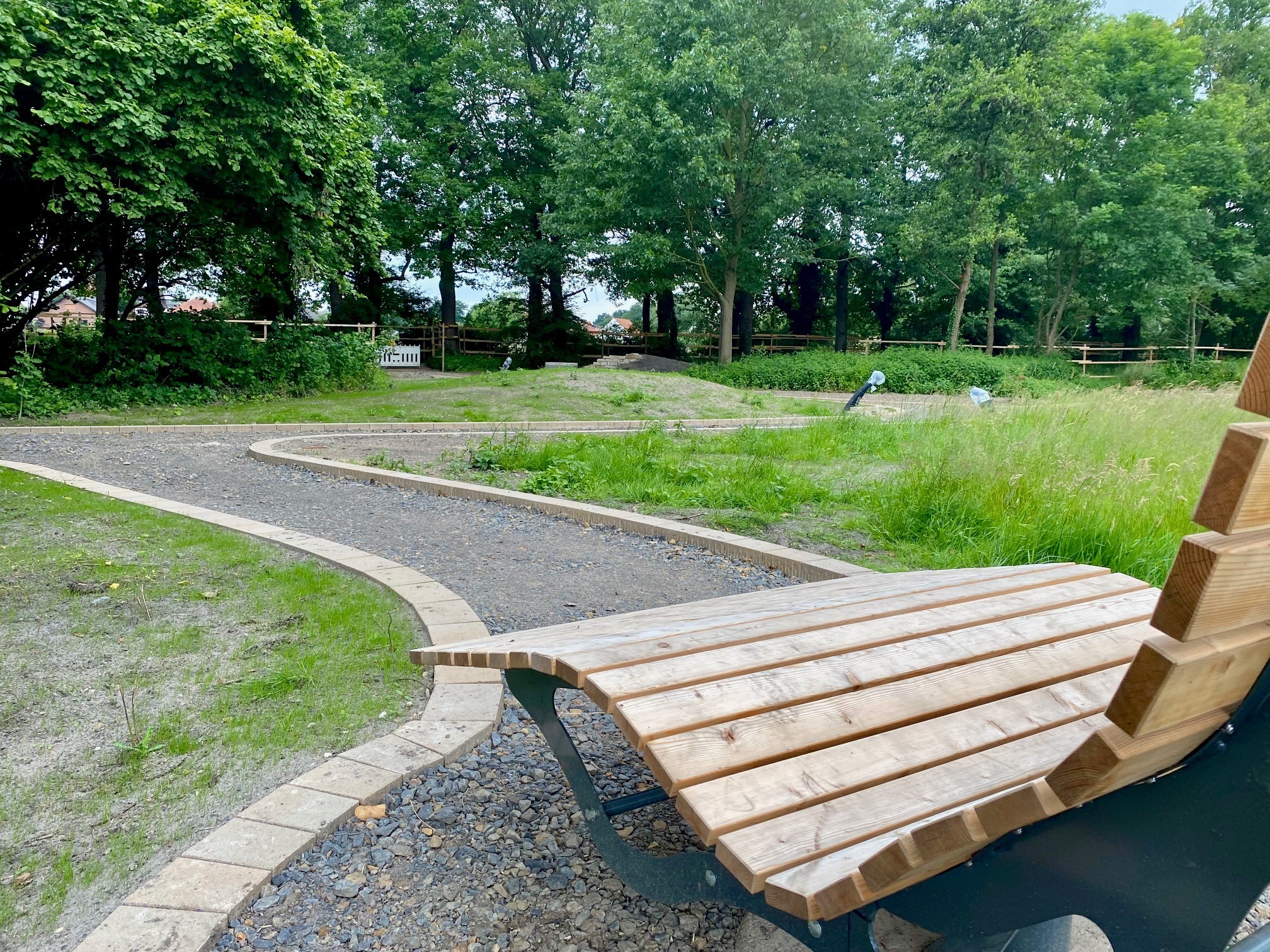 Eine Nahaufnahme einer Holzbank, die in einem Park steht, in dem gerade die Wege und Grünanlagen erneuert werden. 