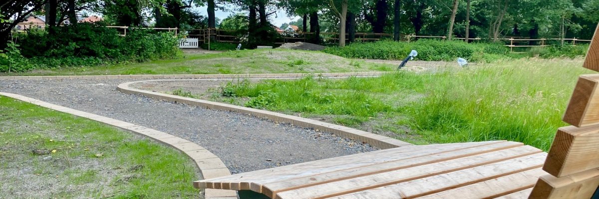 Eine Nahaufnahme einer Holzbank, die in einem Park steht, in dem gerade die Wege und Grünanlagen erneuert werden.