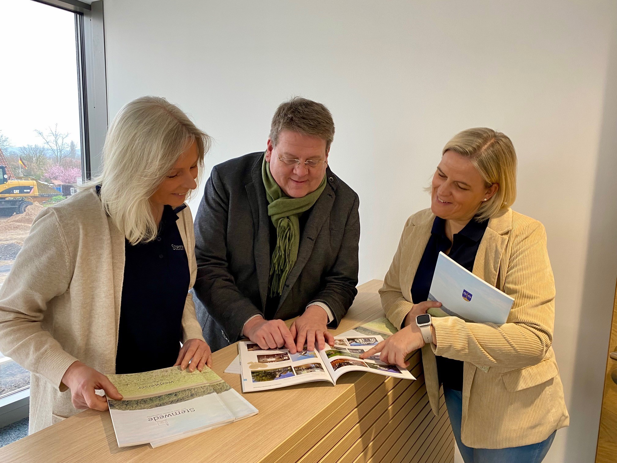 Zwei Frauen und ein Mann stehen an einem Empfangstresen und blättern gemeinsam durch eine Broschüre.