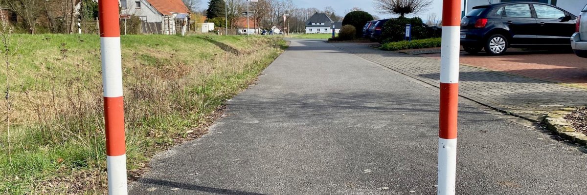 Zwei rot-weiß gestreifte Absperrpfosten, die auf einem geh- und Radweg in einem Wohngebiet stehen.