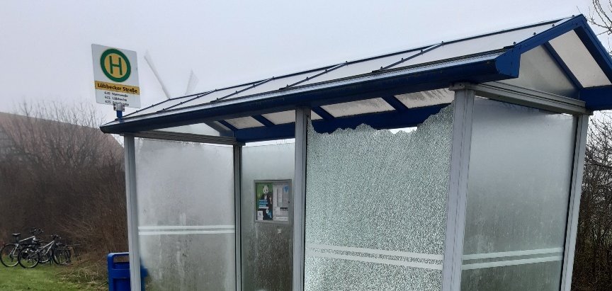 Ein gläsernes Buswartehäuschen, bei dem ein Glaselement zerstört wurde. Es liegen viele Glassplitter herum.