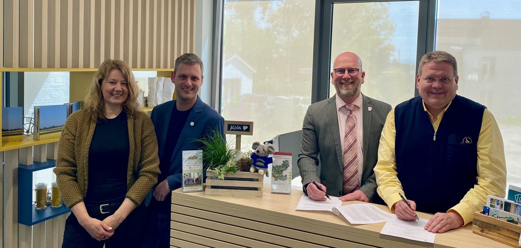 Ein Tourismusbüro mit einer modernen, hölzernen Verkleidung. Eine Frau und drei Männer stehen an einem Empfangstresen und lächeln in die Kamera.