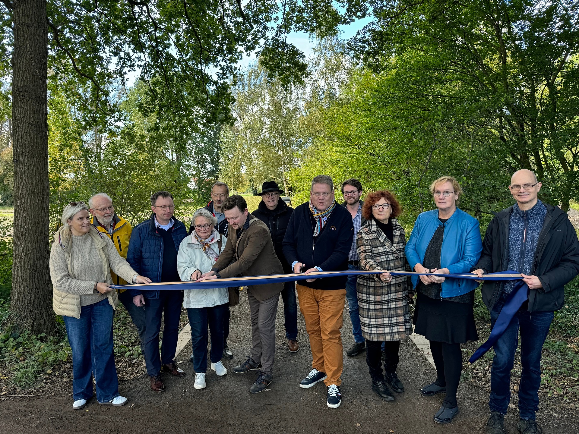 Bürgermeister Kai Abruszat und elf weiterer Personen schneiden symbolisch ein Band durch, um den Kurpark zu eröffnen.